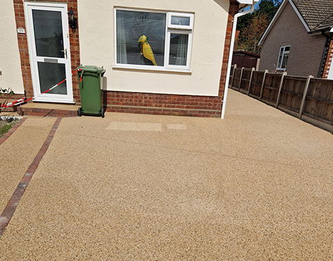 a light brown resin driveway in front of a white and bricked house